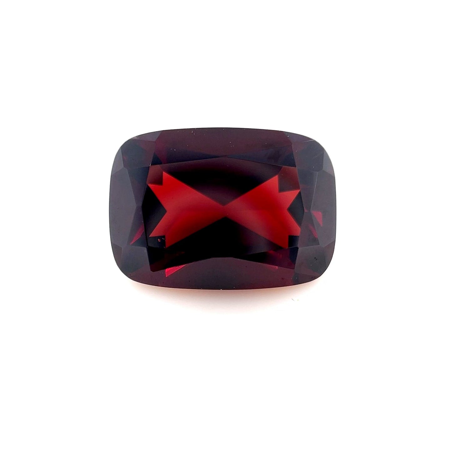 The 14x10mm Cushion Red Garnet has a deep red color and faceted surfaces that reflect light brilliantly, shown on a plain white background.