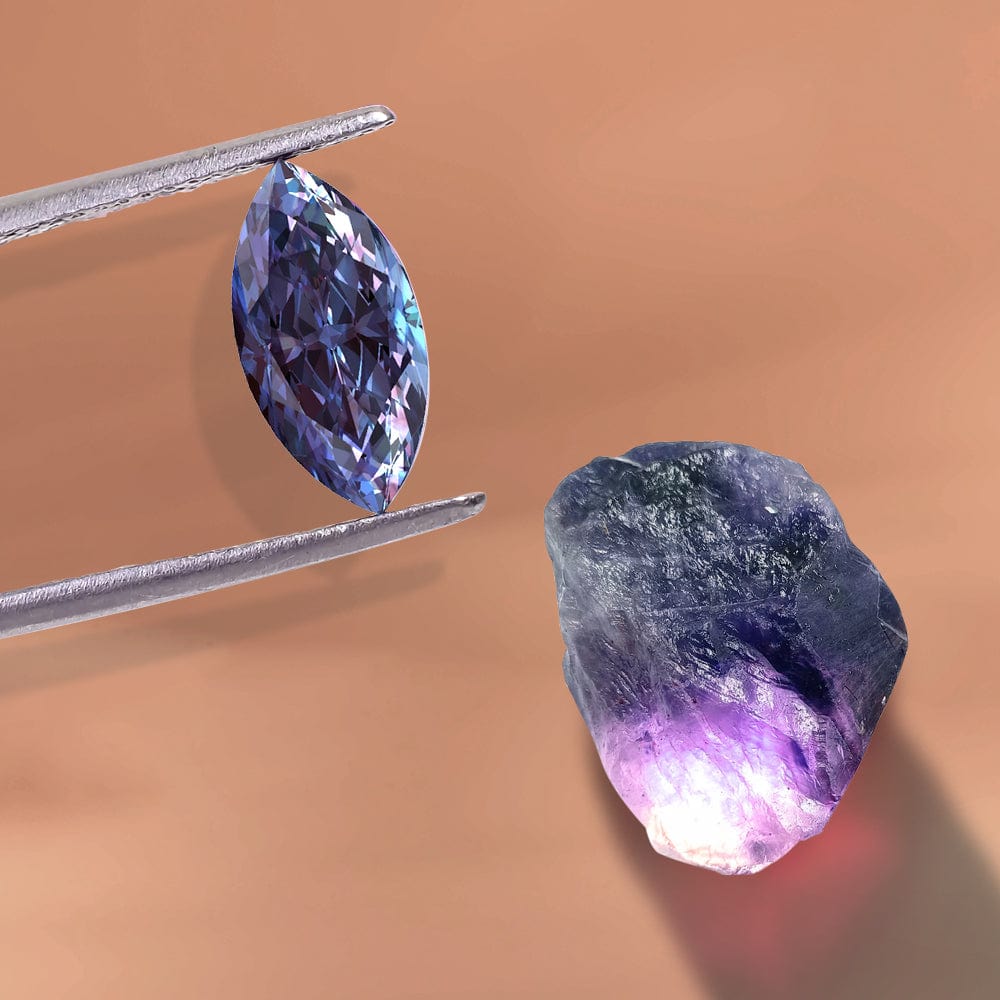 Faceted alexandrite gemstone held by tweezers next to an uncut purple gemstone on a brown background