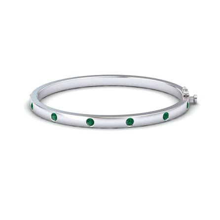 The Emerald Bezel-Set Bracelet - Flavia is a silver bangle adorned with evenly spaced round green gemstones, shown on a white background.