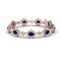 The Ariana Blue Sapphire & Diamond Vintage-Inspired Tennis Bracelet features oval blue sapphires and round white diamonds in an ornate design, showcased on a white background.