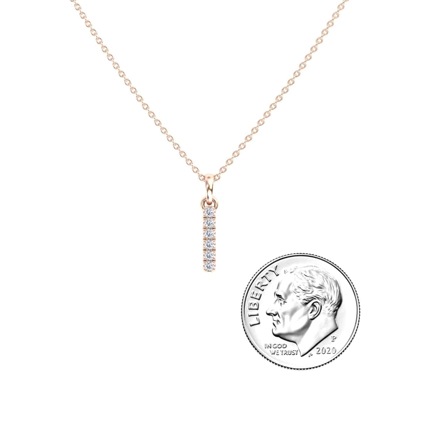 The White Diamond Vertical Bar Necklace - Lalita features a delicate gold chain and a diamond-encrusted vertical bar pendant, displayed next to a U.S. dime for scale.