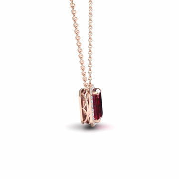 The Ruby & Diamond Halo Necklace - Hilary features an emerald-cut red gemstone pendant in rose gold, displayed at an angle to highlight the side setting and chain on a white background.