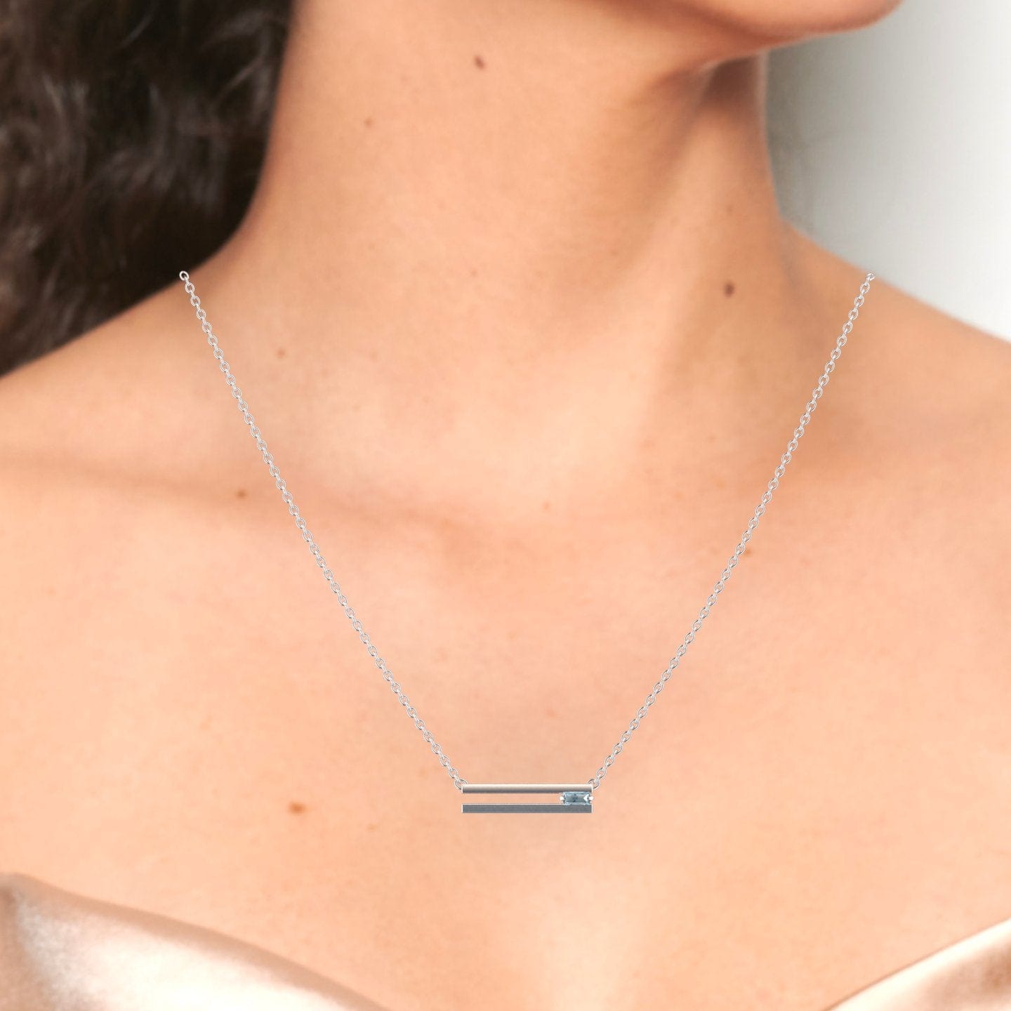 A woman showcases the Cecilia Aquamarine Bar Necklace, a delicate silver chain with a horizontal bar pendant accented by an aquamarine gemstone, paired with a strapless, shimmery top.