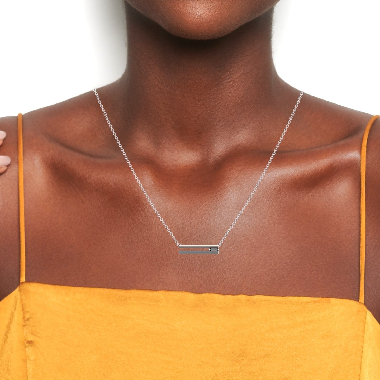 A woman wearing the Cecilia Black Diamond Bar Necklace, a thin silver chain with a horizontal bar pendant, paired with a mustard yellow spaghetti strap top, shown from shoulders to above the chest against a white background.