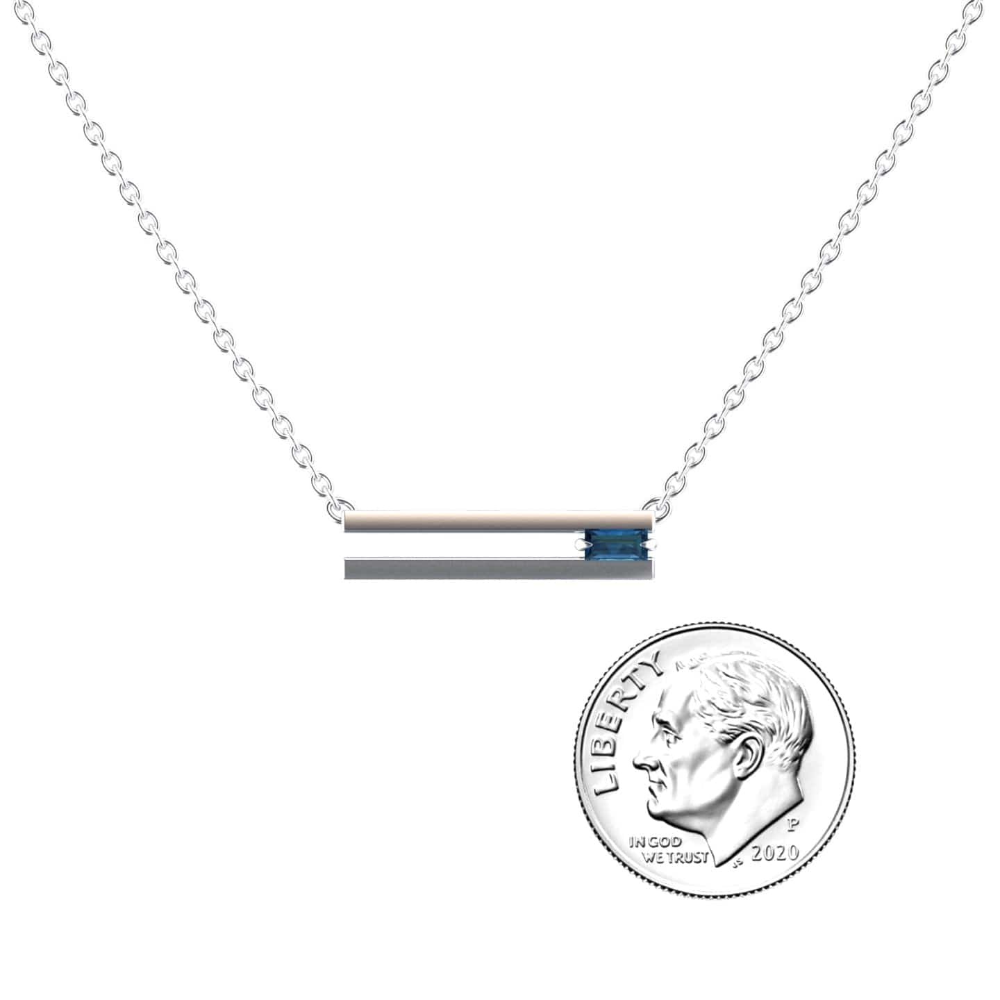 The London Blue Topaz Necklace - Cecilia features a silver chain with a horizontal silver bar pendant and a small blue topaz, shown beside a US dime for size reference.