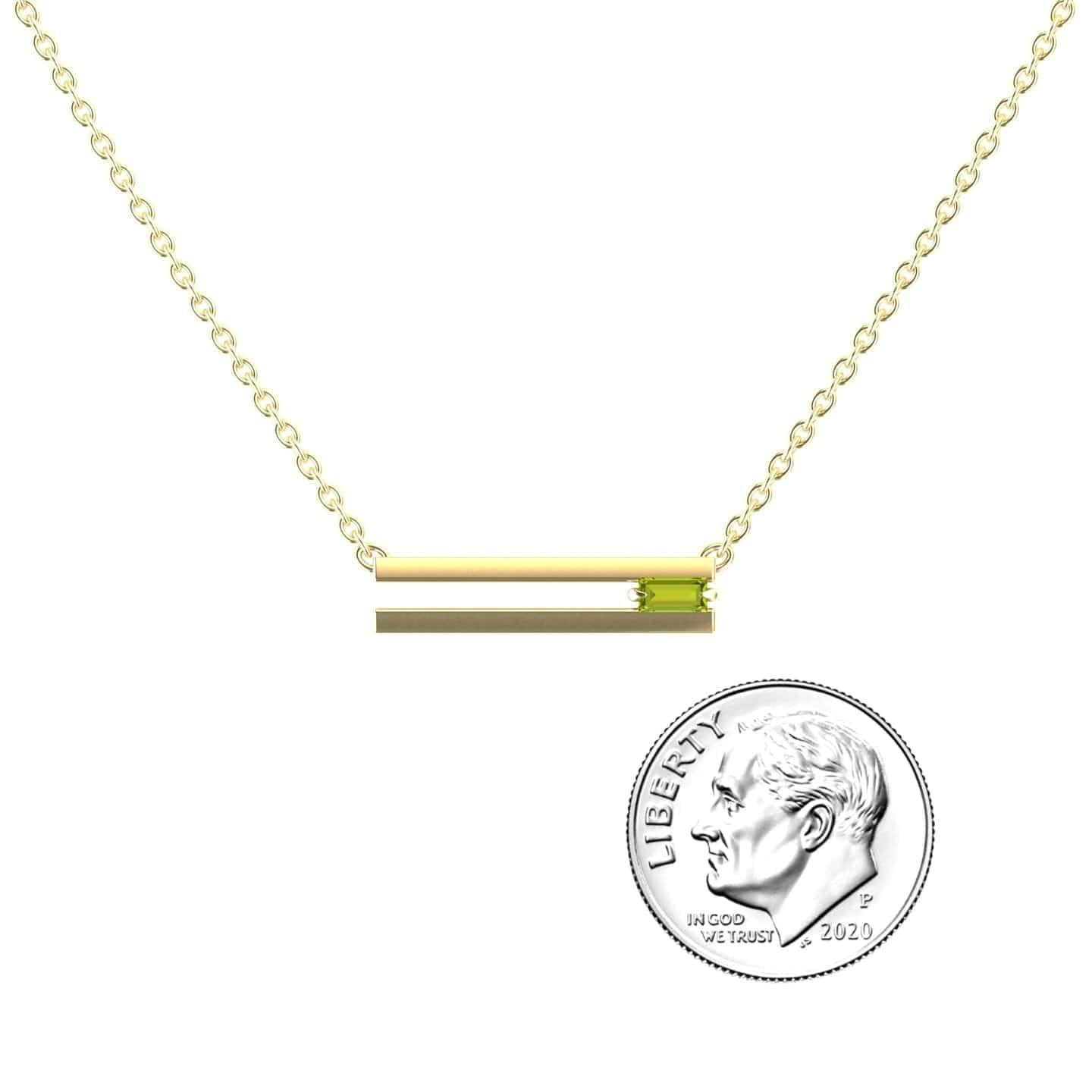 The Peridot Bar Necklace - Cecilia is a gold chain necklace with a horizontal bar pendant and a small green peridot accent, shown beside a 2020 U.S. dime for size comparison.