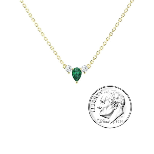 The Emerald & Diamond Three-Stone Necklace - Jina features a delicate gold chain with a teardrop green emerald pendant flanked by two small diamonds, shown beside a US dime for size comparison.