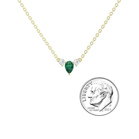 The Emerald & Diamond Three-Stone Necklace - Jina features a delicate gold chain with a teardrop green emerald pendant flanked by two small diamonds, shown beside a US dime for size comparison.