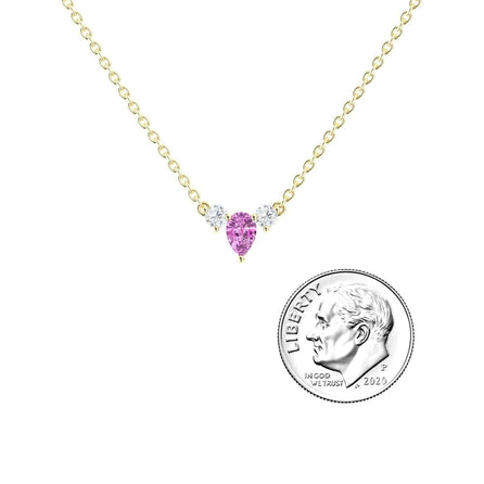 The Pink Sapphire & Diamond Three-Stone Necklace - Jina features a gold chain with a pink sapphire pear center and two small diamonds, shown beside a U.S. dime for size reference.