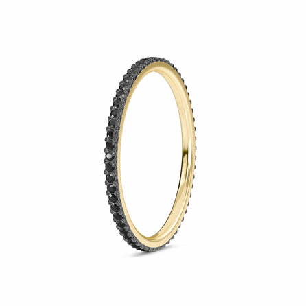 The Black Diamond Ballad Eternity Ring - Colleen features a slim gold band adorned with a full circle of small black stones, displayed on a white background.
