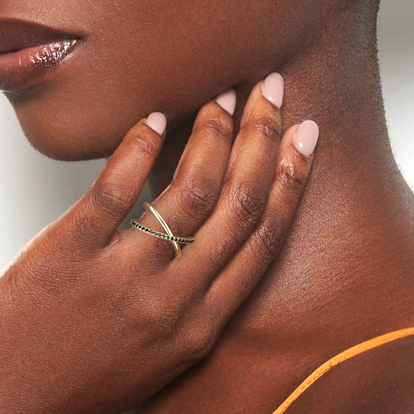 A close-up of a hand with nude nails rests on a neck, highlighting the Trisha Black Diamond Criss-Cross Pave Band Ring against smooth skin and a mustard-colored top.