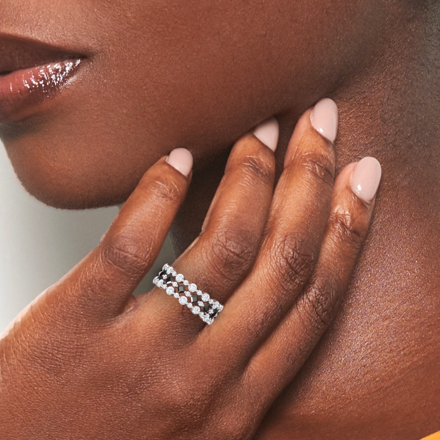 A close-up of a person with dark skin wearing the Black & White Diamond Lace Band Ring - Victoria. Their nails are manicured in light nude and their lips have a glossy sheen.