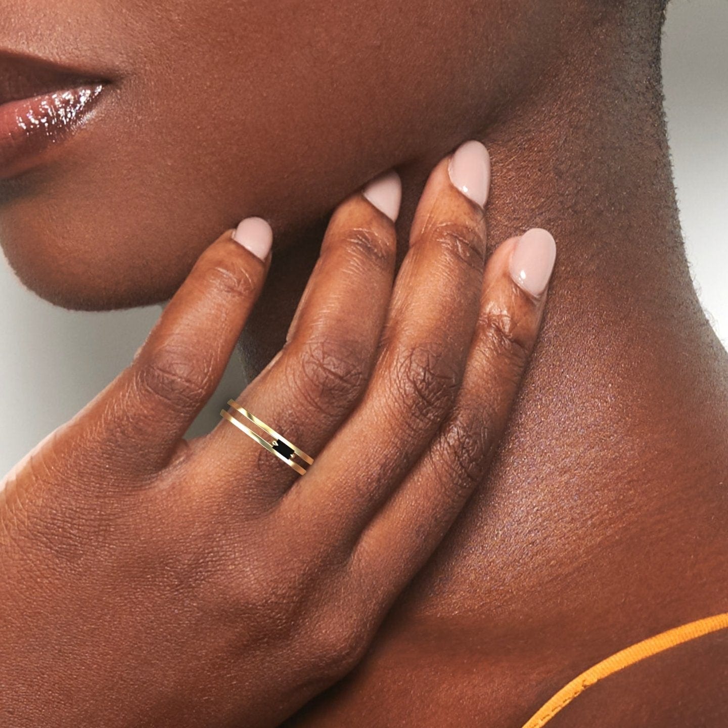 A close-up of a hand resting on a neck, featuring nude manicured nails and the Black Diamond Minimalist Double Band Ring - Alia. The image highlights smooth skin and glossy, dark lips.