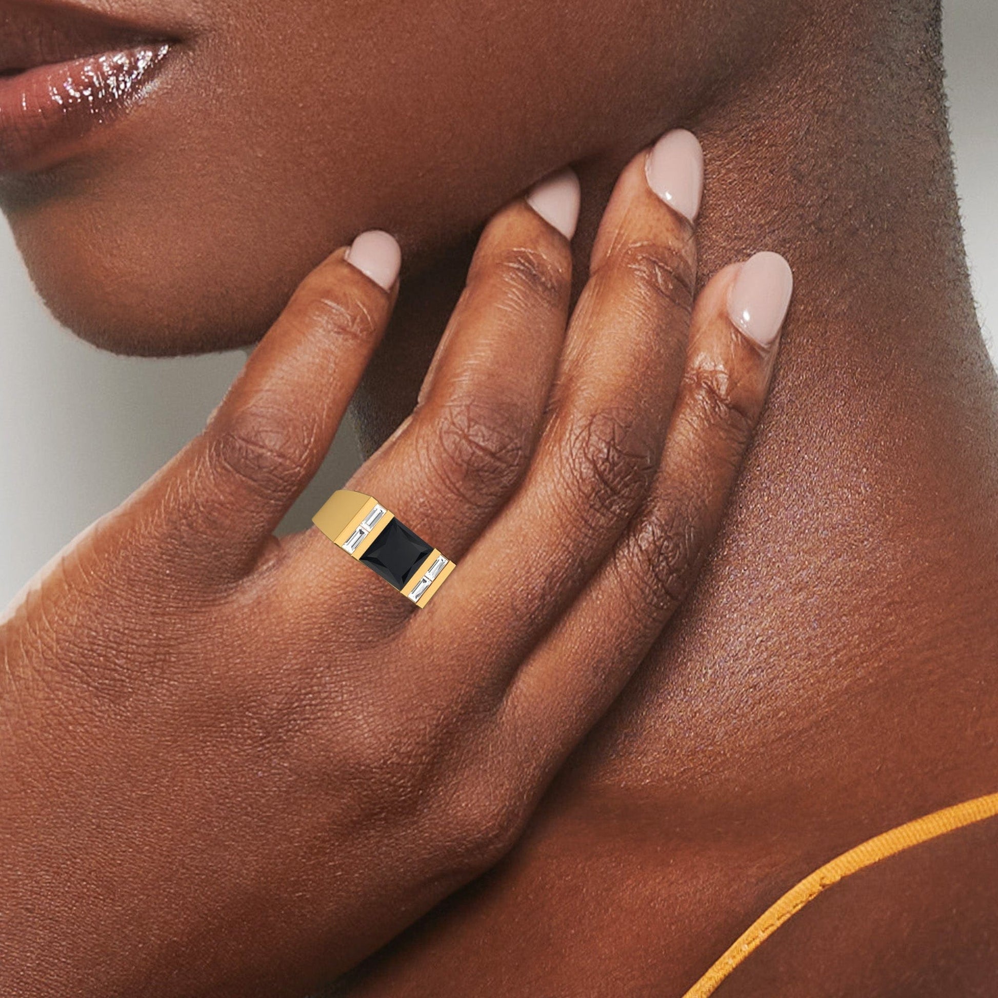 A close-up of a person with smooth dark skin and nude-colored nails touches their neck, showcasing the Black & White Diamond Mens Statement Ring - Casper on their finger. They are also wearing a yellow strap.