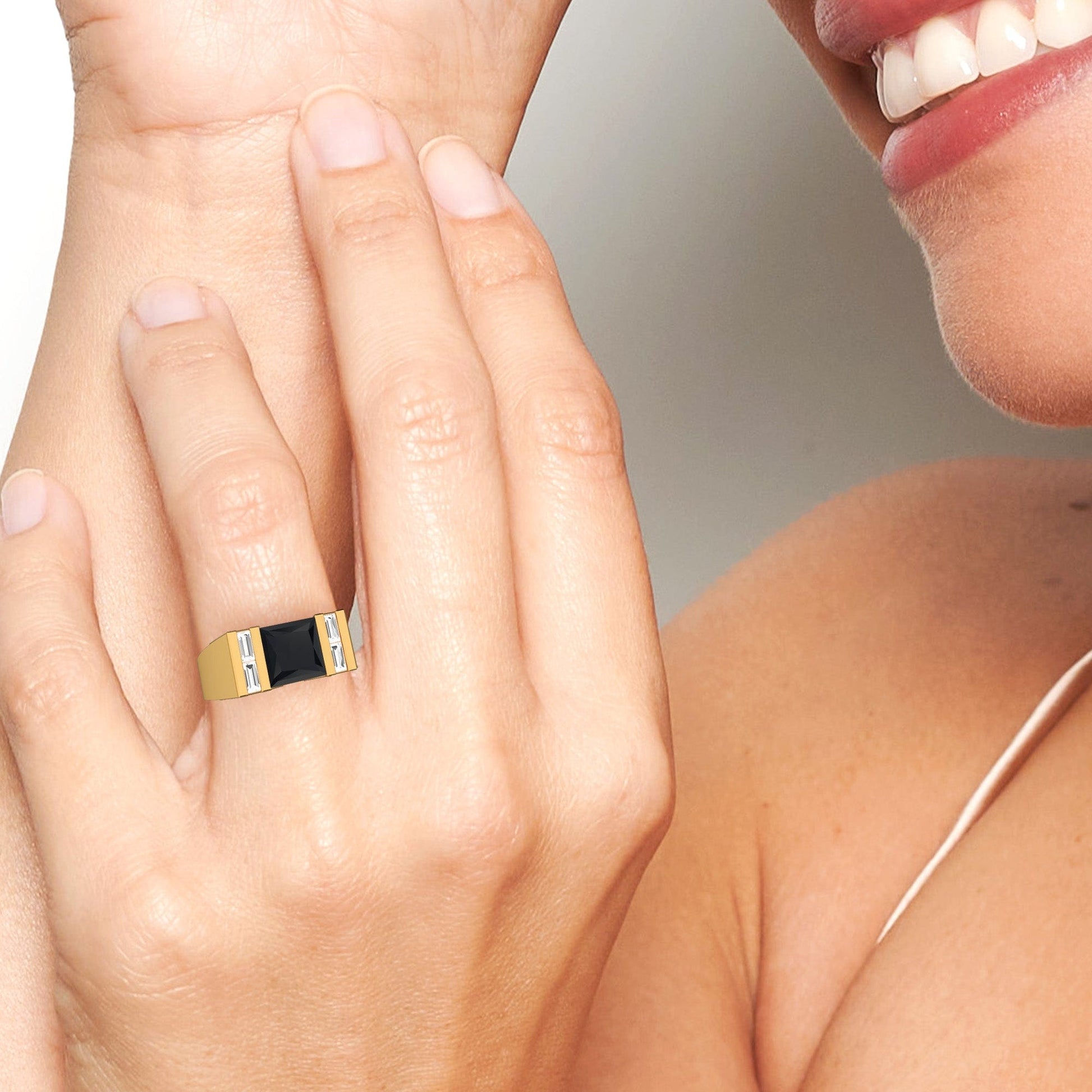 A smiling person wears the Casper Black & White Diamond Mens Statement Ring, featuring a black rectangular stone and silver accents, while gently touching their face.