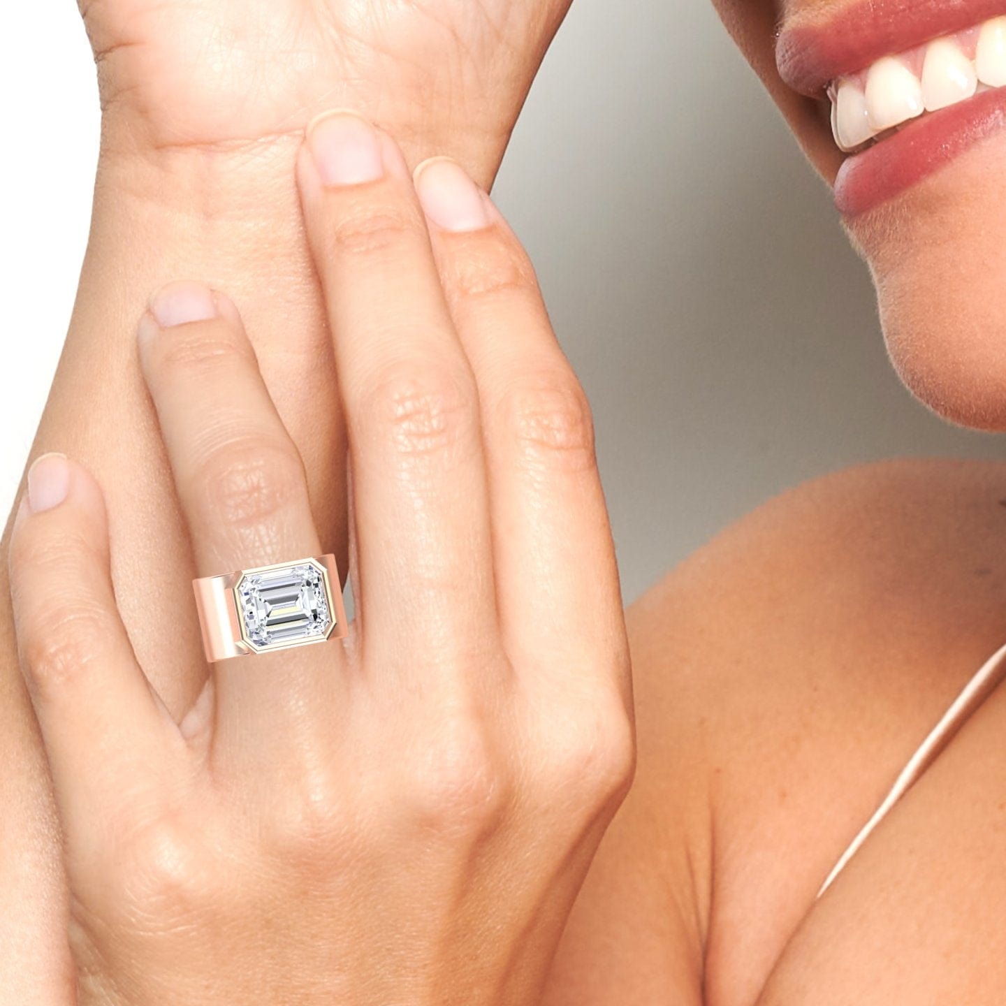 A smiling person displays the Moissanite Statement Ring - Aparna, featuring a large emerald-cut stone and wide band, while holding their hand near their face.