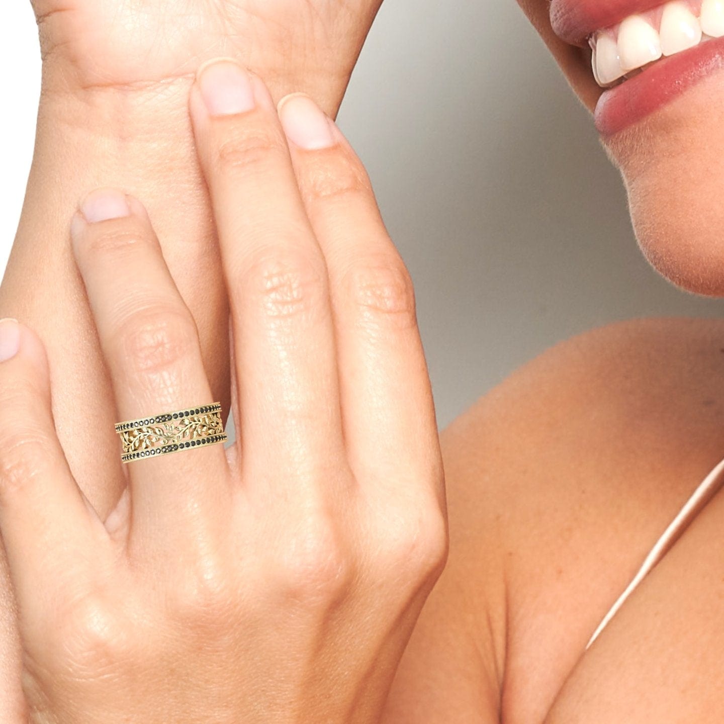 Smiling, a person displays the Black Diamond Vine Motif Eternity Band – Casey on their ring finger, their hand near their face to showcase the band’s elegant design.