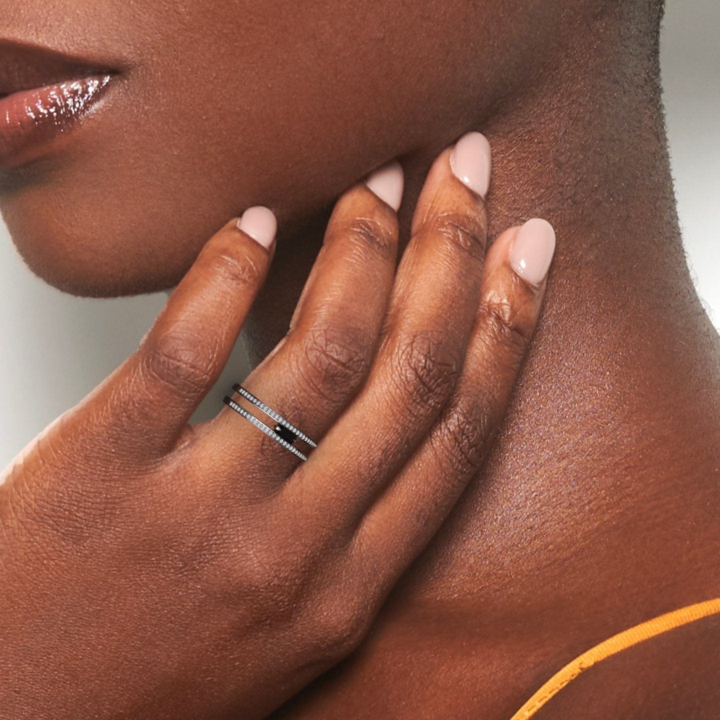 A womans hand with smooth skin and nude nails gently touches her neck, highlighting the Bianca Black & White Diamond Double Band—two stacked silver rings with small stones. She wears a thin orange strap.