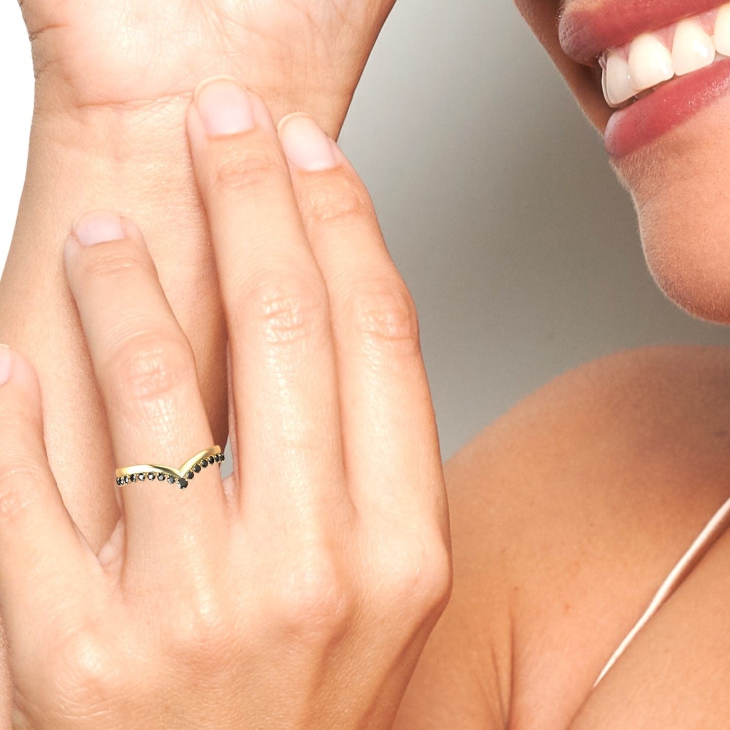 A person smiles while touching their face, showcasing the Black Diamond Cybelle Chevron Wedding Band - Yizhen on their finger. The photo highlights their hand, the ring, and a glimpse of their face and shoulder.