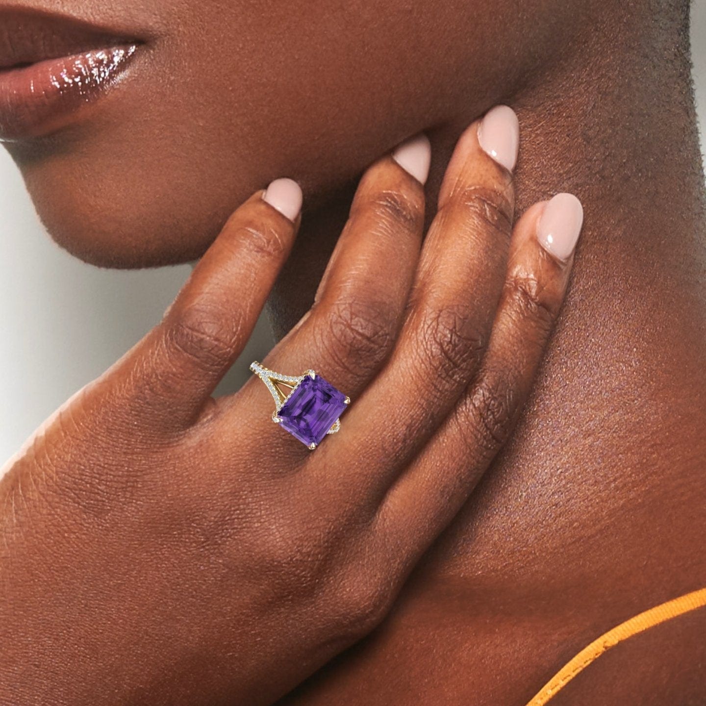 A close-up of a womans hand with manicured nails, wearing the Amethyst & Diamond Cocktail Ring - Ziya, featuring a large rectangular purple gemstone set in silver, gently resting on her neck and jawline.