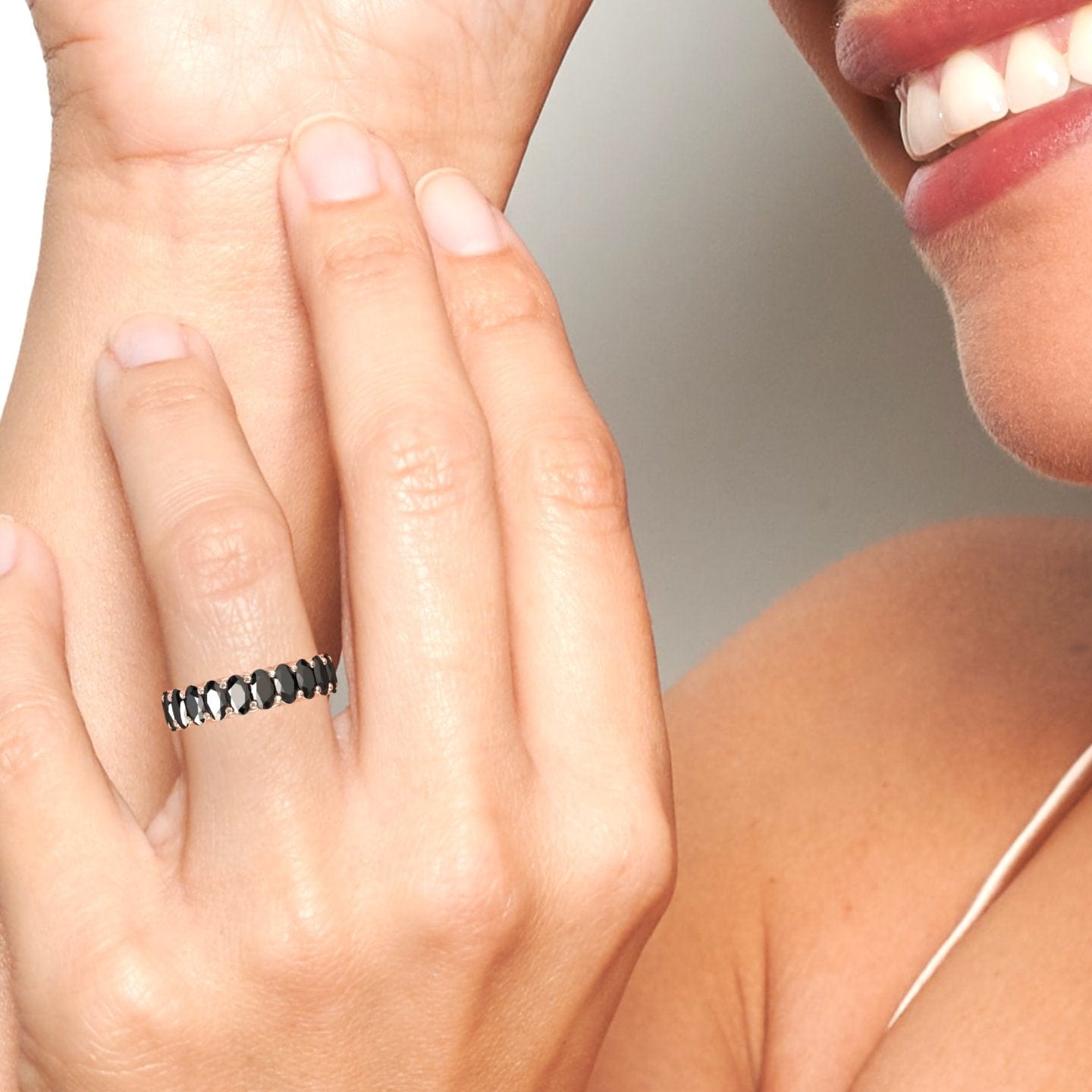 A person smiling and touching their face, showcasing the Black Diamond Full Eternity Band - Diana on their finger. The image highlights the hand, ring, and part of their face and shoulder.