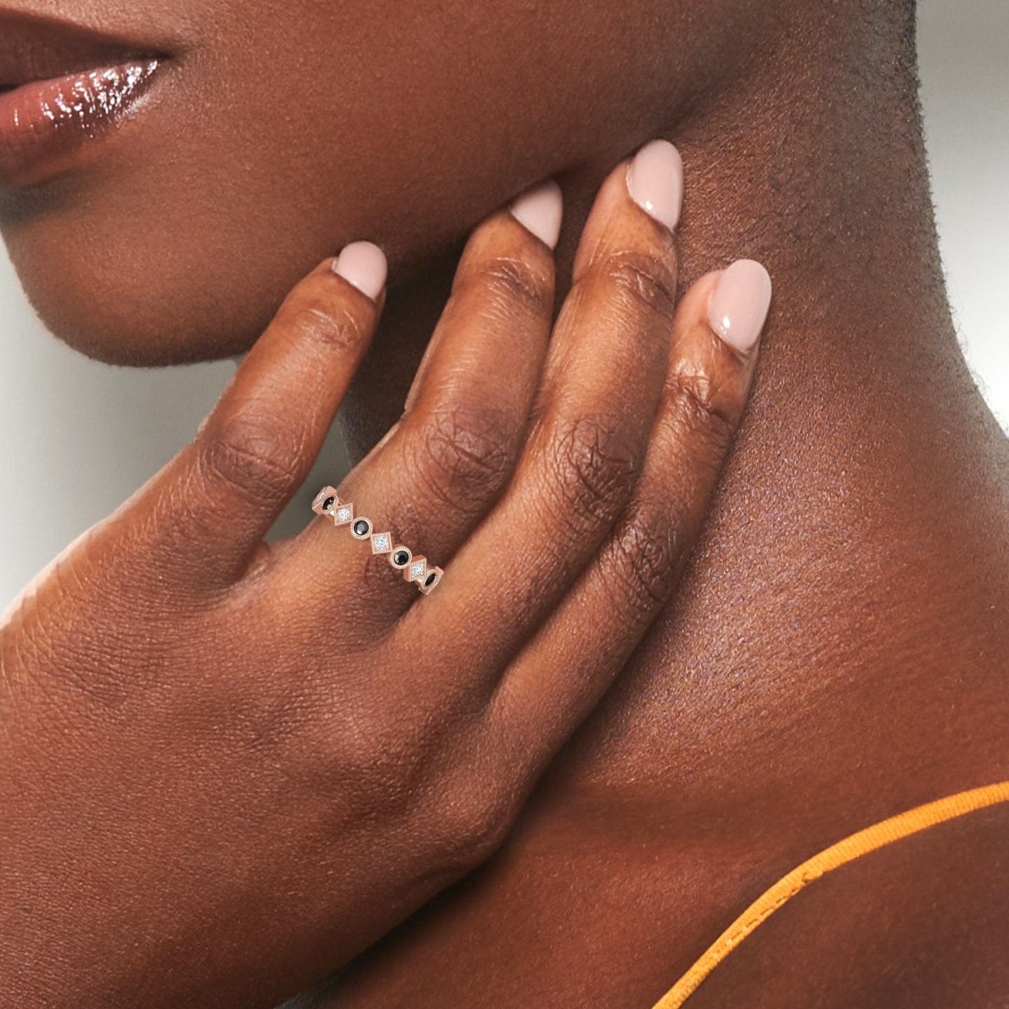 A close-up of a womans hand with smooth brown skin and nude nails, wearing a mustard yellow strap and the Hetal Black & White Diamond Geometric Eternity Band—a delicate ring featuring small black and white diamonds.