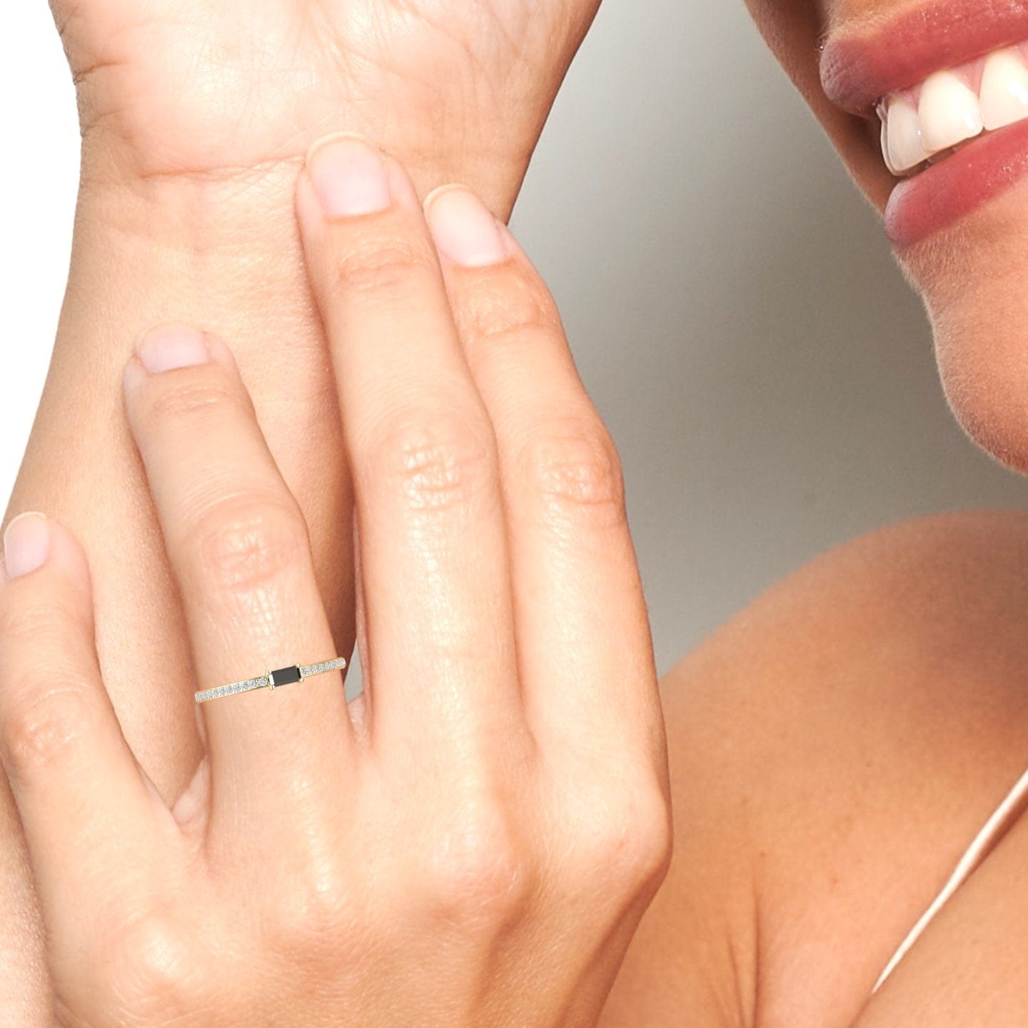 A close-up shows a smiling person touching their cheek, wearing the Black & White Diamond Pave Ring - Dia—a thin, elegant band with small stones and a black rectangular accent on their finger.
