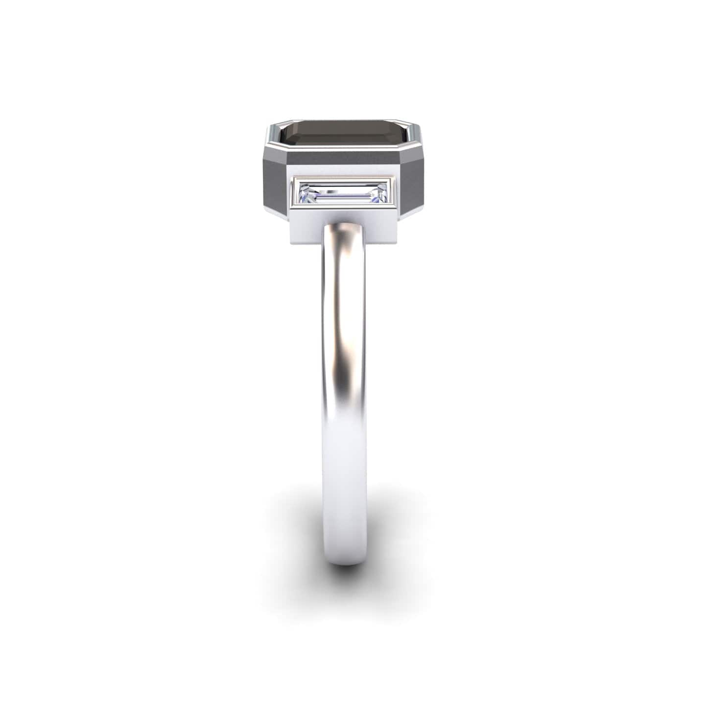 The Black & White Diamond Three-Stone Art Deco Ring - Ivy features a rectangular dark gemstone in a bezel setting with a clear baguette-cut accent, displayed from the side on a simple white background.