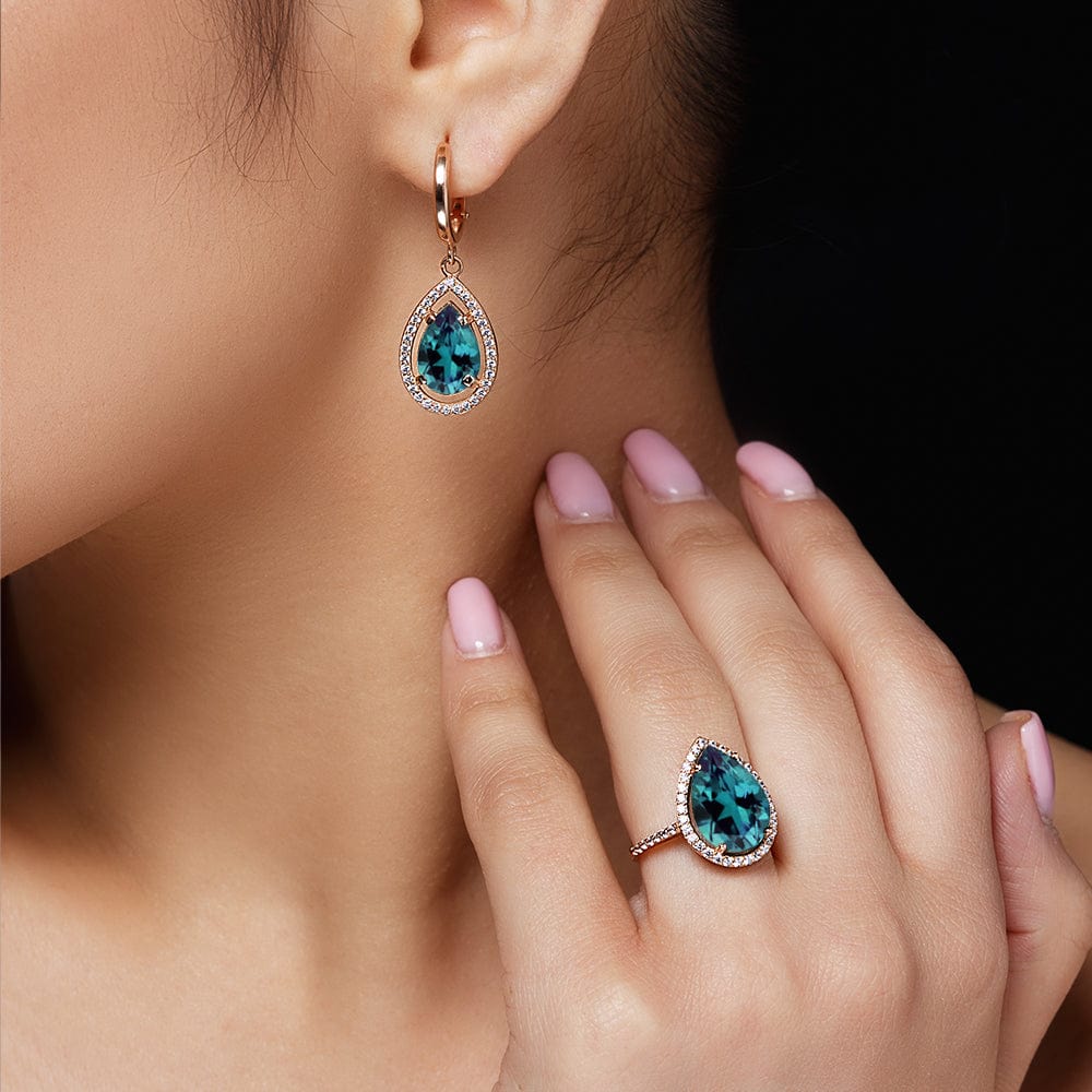 Teardrop-shaped alexandrite gemstone earrings and ring on a model's hand and ear.