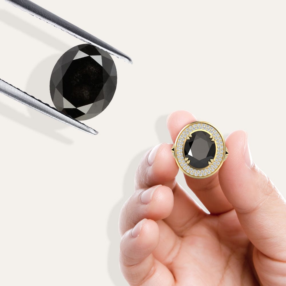 Gold ring with a black diamond held by a hand against a white background