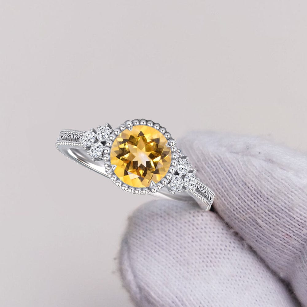Silver ring with a yellow citrine gemstone held by a gloved hand on a light gray background