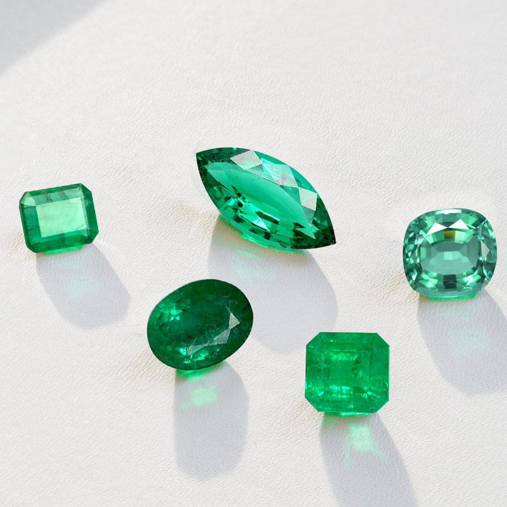 Five emerald gemstones of different shapes and sizes on a light background