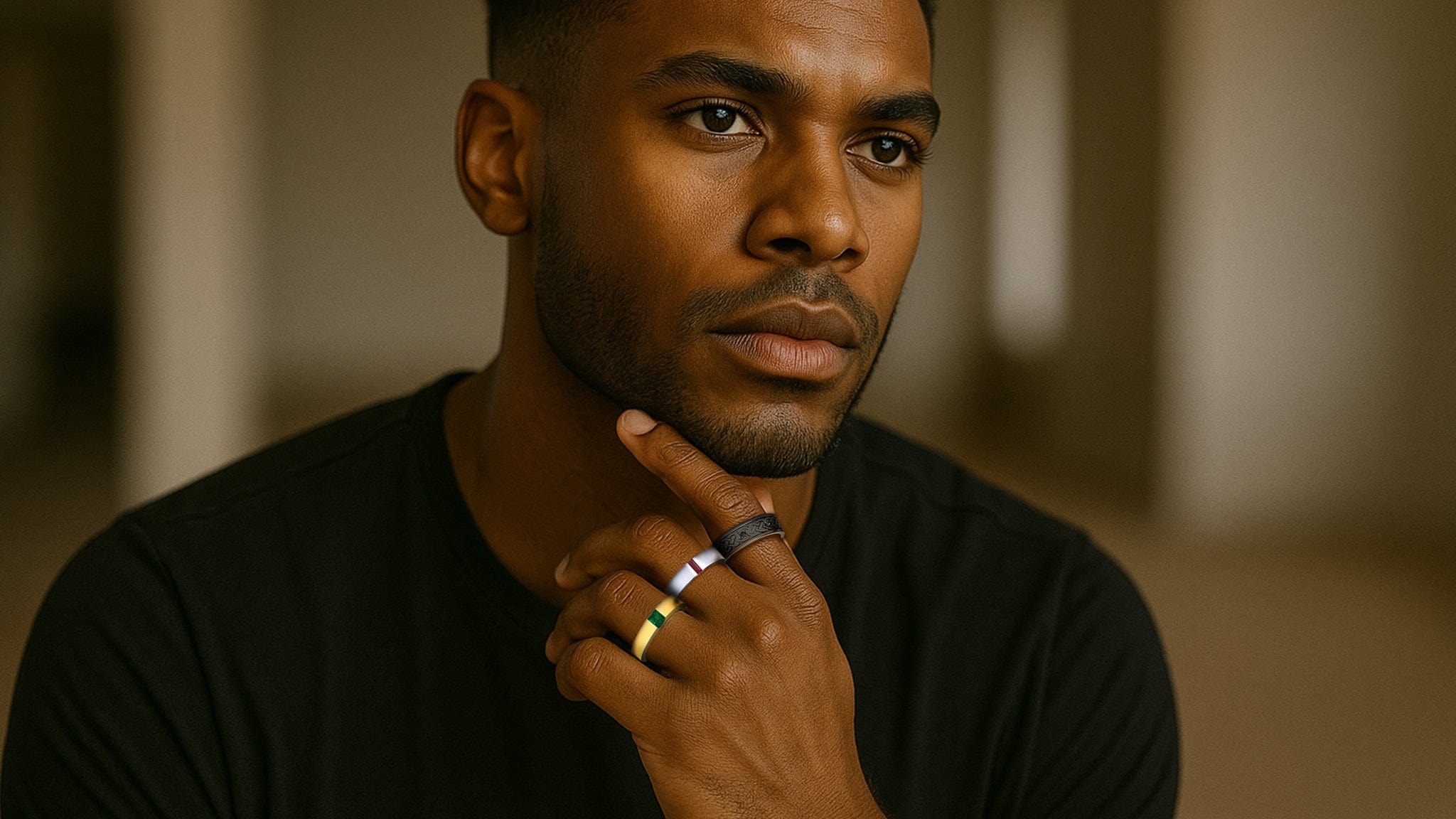 Man with a thoughtful expression, wearing rings, in a blurred indoor setting