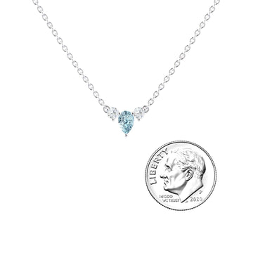 The Aquamarine & Diamond Three-Stone Necklace - Jina features a teardrop-shaped blue aquamarine pendant flanked by two diamonds, displayed beside a 2020 U.S. dime for size reference on a white background.