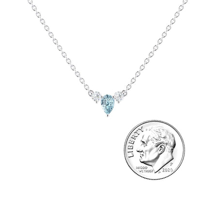 The Aquamarine & Diamond Three-Stone Necklace - Jina features a teardrop-shaped blue aquamarine pendant flanked by two diamonds, displayed beside a 2020 U.S. dime for size reference on a white background.