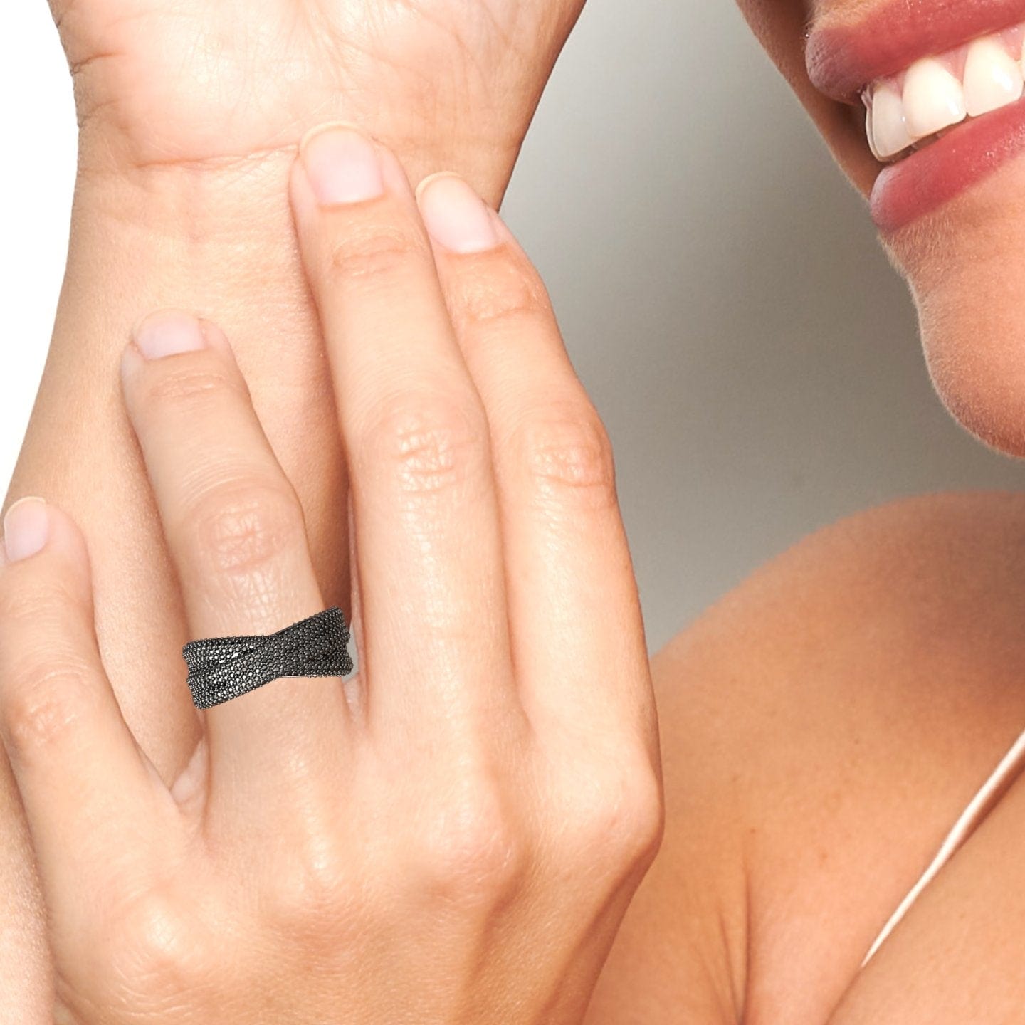 A person smiles, touching their face and highlighting the Black Diamond Pave Crossover Statement Ring - Noor on their finger. The photo centers on the hand, ring, and part of the persons mouth and chin.