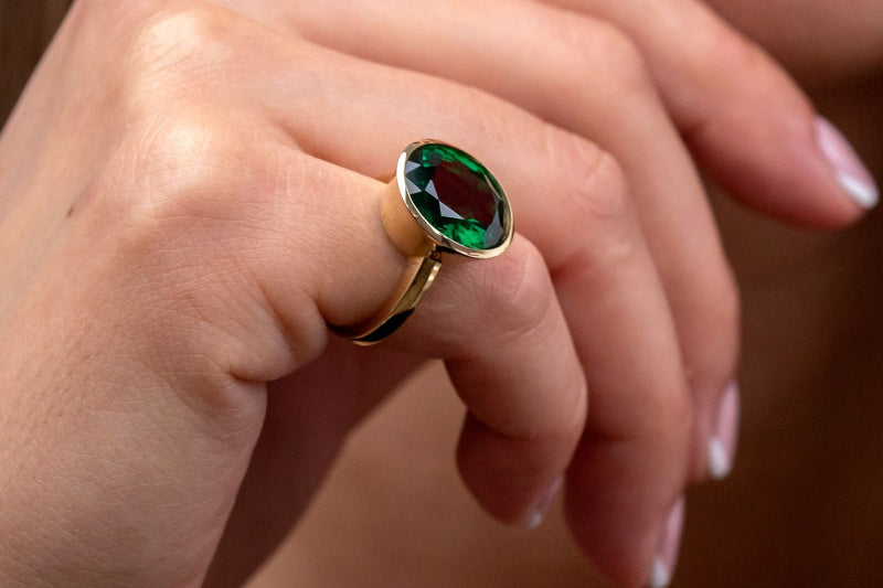 The pinky finger adorned with an emerald ring.
