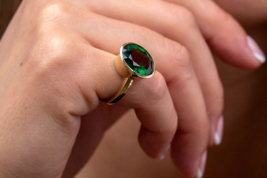 The pinky finger adorned with an emerald ring.
