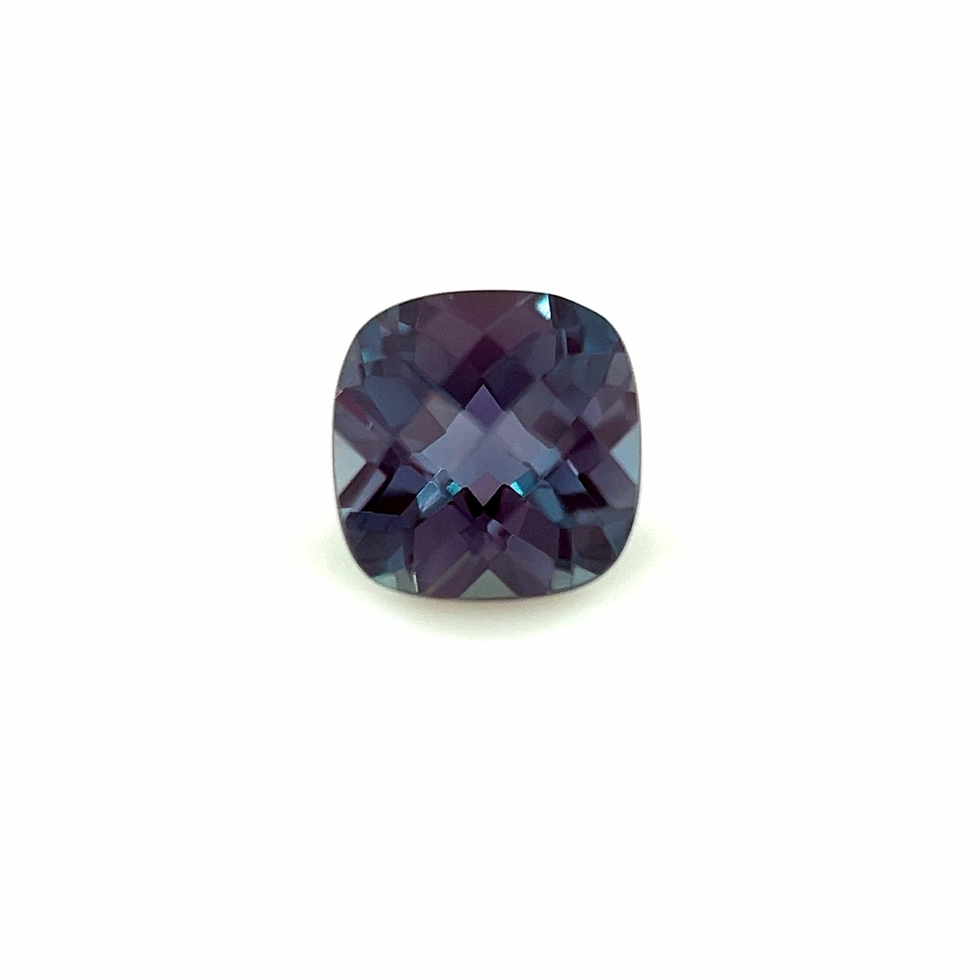 The 8.0x6.0 Exceptional Cushion Lab Created Alexandrite is a cushion-cut gemstone with deep blue and purple hues and multiple light-reflecting facets, displayed on a plain white background.