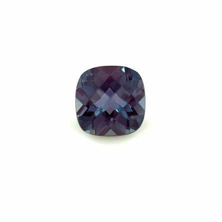 The 8.0x6.0 Exceptional Cushion Lab Created Alexandrite is a cushion-cut gemstone with deep blue and purple hues and multiple light-reflecting facets, displayed on a plain white background.