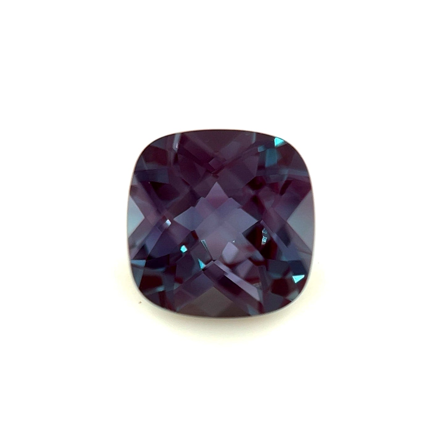 The 7mm Exceptional Cushion Checker Lab Created Alexandrite features a cushion cut and checkerboard facets in deep purple, shown against a white background.