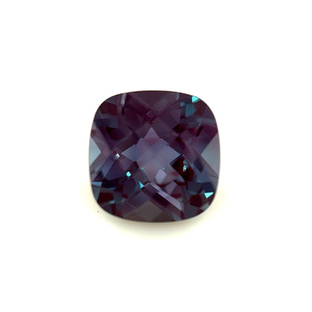 The 7mm Exceptional Cushion Checker Lab Created Alexandrite features a cushion cut and checkerboard facets in deep purple, shown against a white background.