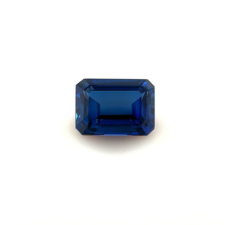 The 7.0x5.0 Exceptional Emerald Lab Created Blue Sapphire features a deep blue color and sharp, faceted edges, beautifully showcased against a plain white background.