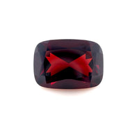 The 14x10mm Cushion Red Garnet has a deep red color and faceted surfaces that reflect light brilliantly, shown on a plain white background.