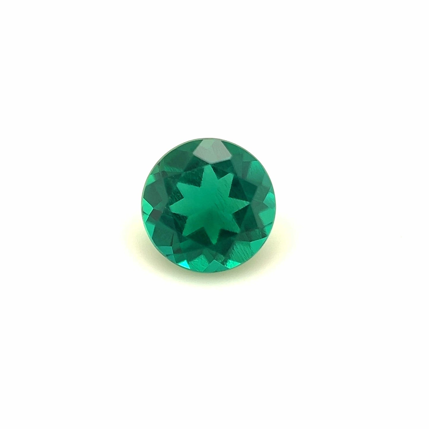 The 6mm Exceptional Round Zambian Color Lab Created Emerald features a vivid green hue and a unique star-shaped pattern at its center, shown against a plain white background.