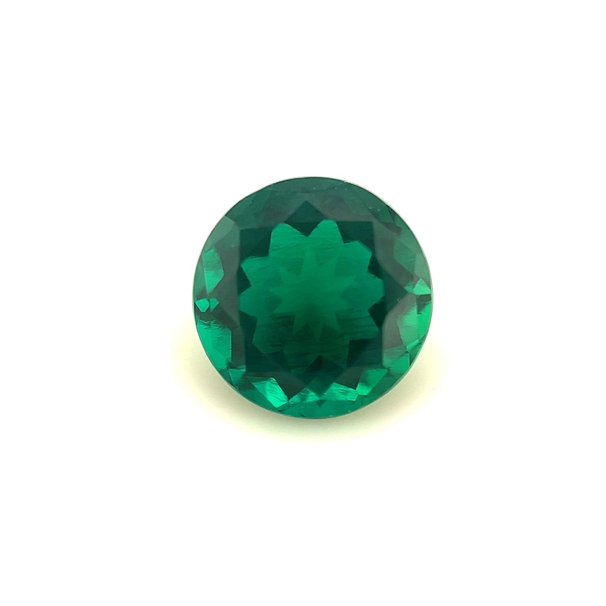 An 8mm Exceptional Round Zambian Color Lab Created Emerald, showcasing a symmetrical star-like pattern at its center, is displayed on a plain white background.