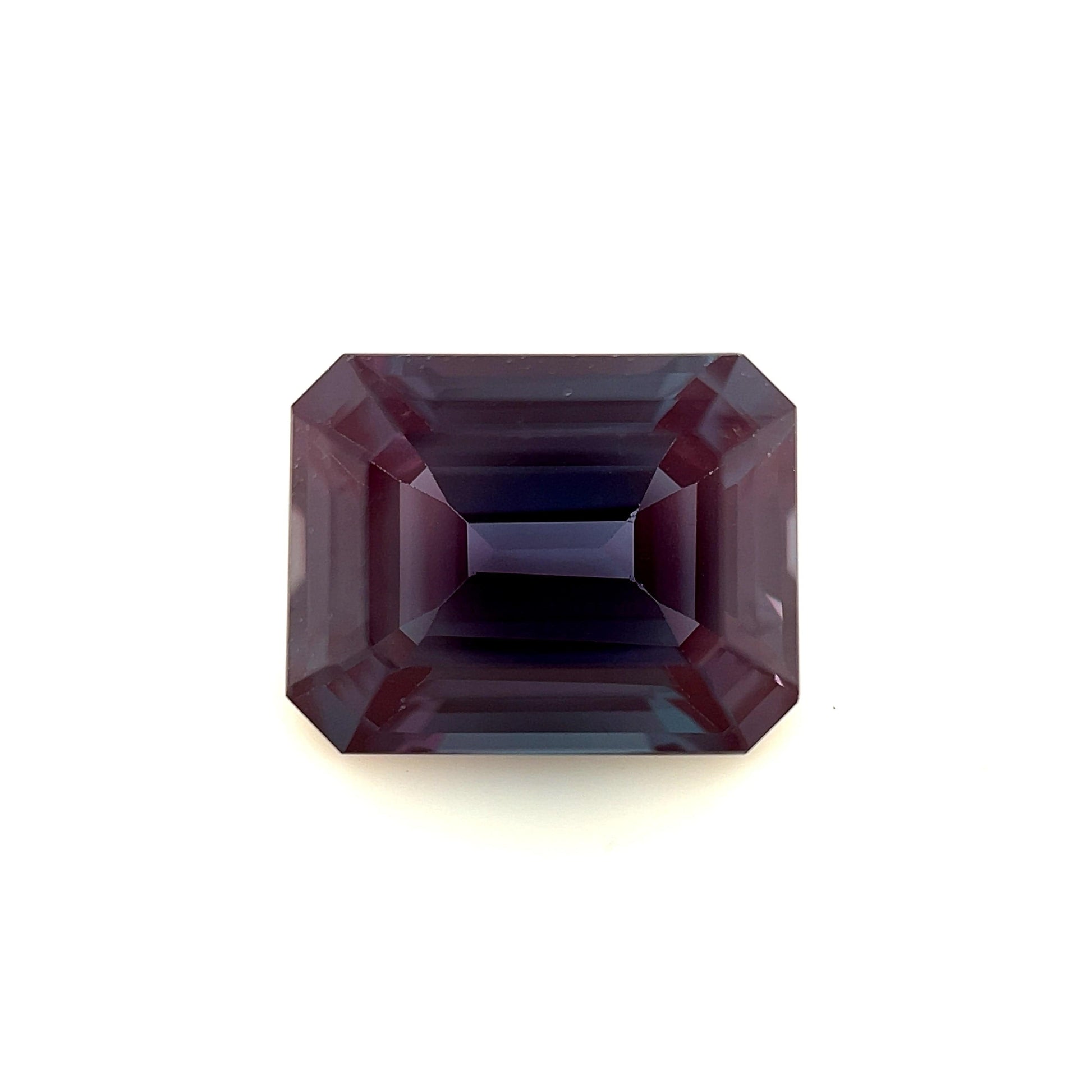 A 10.0x8.0 exceptional emerald-cut lab created Alexandrite with deep purple hues and sharp facets is displayed against a plain white background.