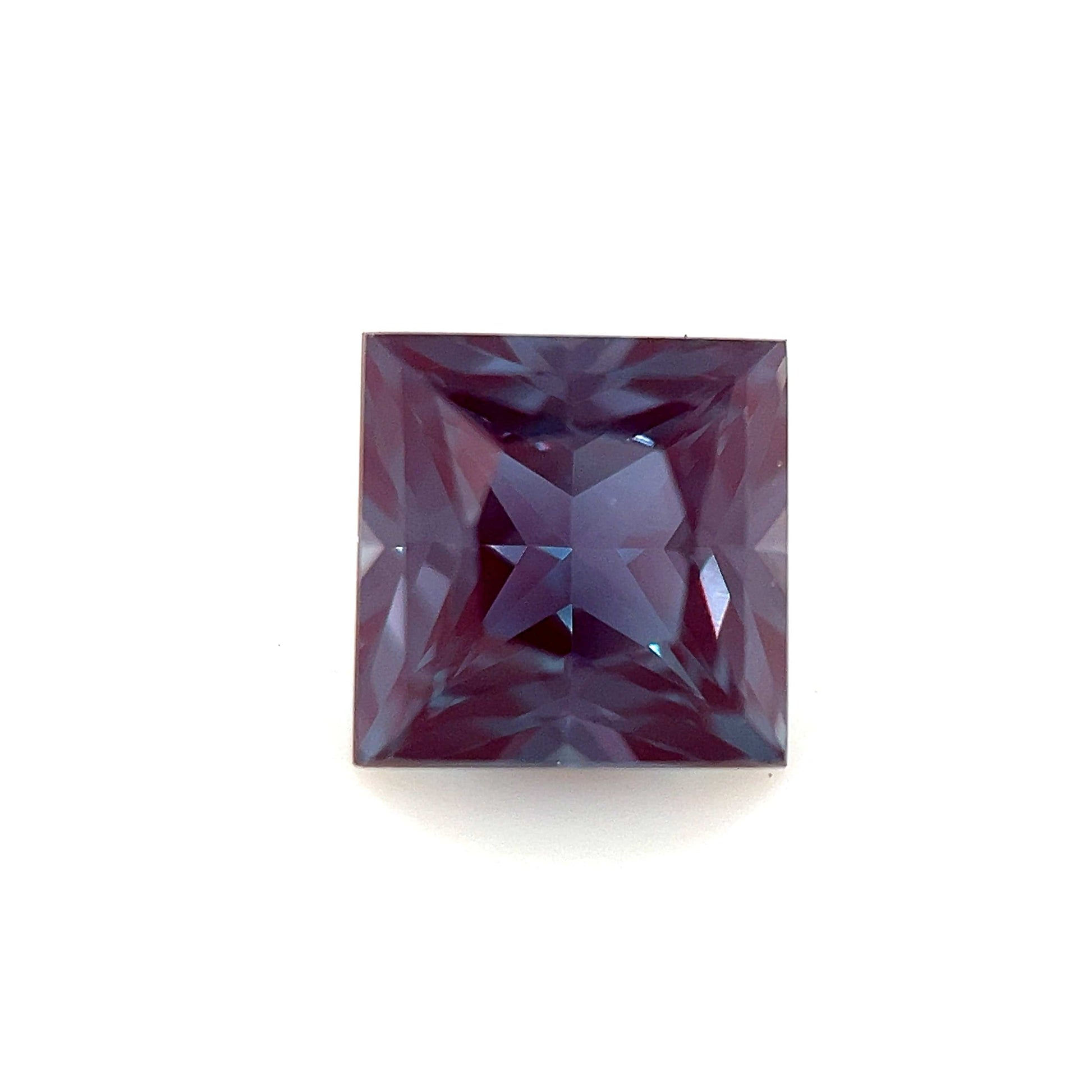 A 6mm Exceptional Square Princess Lab Created Alexandrite, with a deep purple hue and faceted surface, is shown against a plain white background.