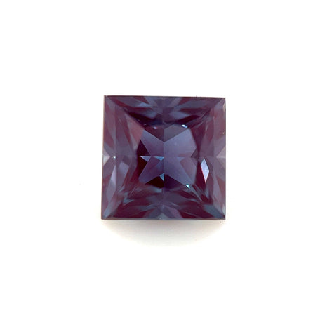 A 6mm Exceptional Square Princess Lab Created Alexandrite, with a deep purple hue and faceted surface, is shown against a plain white background.