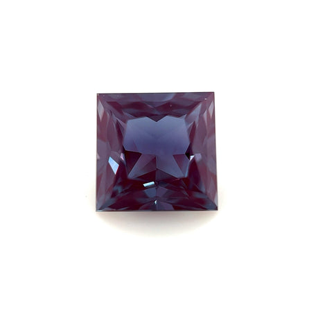 The 7mm Exceptional Square Princess Lab Created Alexandrite features a striking deep blue-purple hue and intricate faceted edges, displayed on a plain white background to highlight its symmetrical princess cut and radiant lab-created brilliance.